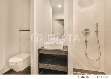 Modern flush toilet and ceramic sink installed on white tiled walls near shower box and mirror n small restroom at home Modern flush toilet and ceramic sink installed on white tiled walls near shower box and mirror n small restroom at home 90164098