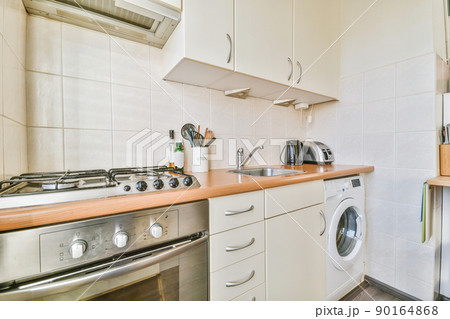 Fragment of interior of light narrow home kitchen with minimalist style white furniture with sink and stove 90164868