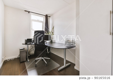 Comfortable chair placed near desk with computer monitor located close to small window in light workplace in modern apartment 90165016