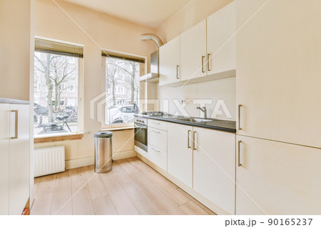 Fragment of interior of light narrow home kitchen with minimalist style white furniture with sink and stove Fragment of interior of light narrow home kitchen with minimalist style white furniture with sink and stove 90165237