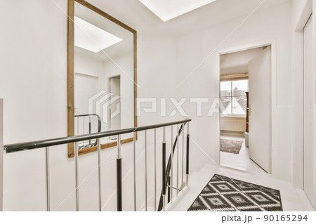 The second floor of a residential building with a large square mirror above the stairs The second floor of a residential building with a large square mirror above the stairs 90165294
