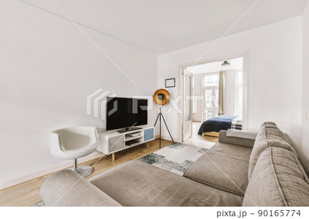 Corner grey sofa on the opposite side of the TV on a stand, armchair and lamp and the entrance to the bedroom 90165774