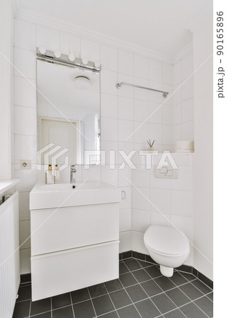 Modern flush toilet and ceramic sink installed on white tiled walls near mirror and towel in small restroom at home 90165896