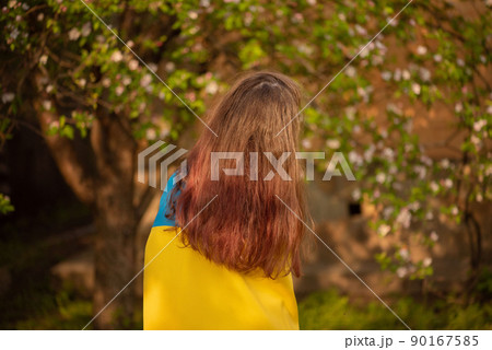 Yellow and blue fabric on the girl. Teen girl is standing with the Ukrainian flag. 90167585
