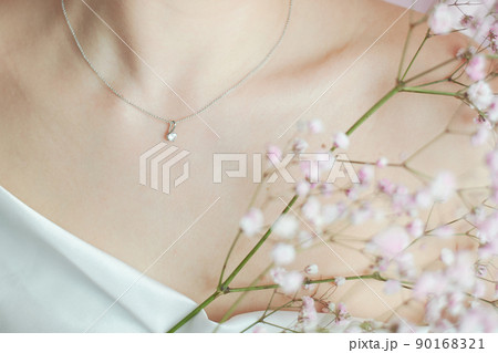 A sprig of pink hippophile, a woman's neck and a silver jewelry with a transparent stone. Tenderness in the advertising of jewelry and perfume. Beauty and women's health. 90168321