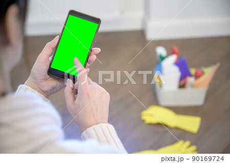 a woman holds a phone against the background of a plastic basket with detergents, brushes, sponges and rubber gloves for cleaning. a woman holds a phone against the background of a plastic basket with detergents, brushes, sponges and rubber gloves for cleaning. 90169724