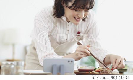 スマホを見ながら料理をする若い女性 90171439