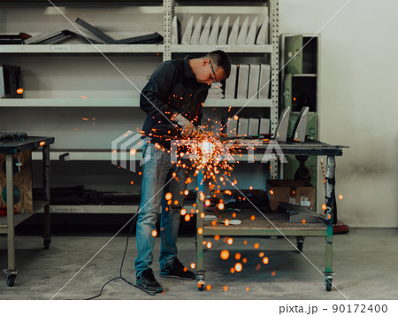 Heavy Industry Engineering Factory Interior with Industrial Worker Using Angle Grinder and Cutting a Metal Tube. Contractor in Safety Uniform and Hard Hat Manufacturing Metal Structures. Heavy Industry Engineering Factory Interior with Industrial Worker Using Angle Grinder and Cutting a Metal Tube. Contractor in Safety Uniform and Hard Hat Manufacturing Metal Structures. 90172400