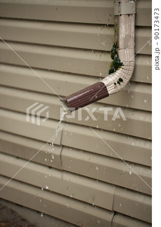 Rain Water Pours Out of a Short Downspout on side of house pooling by foundation 90173473