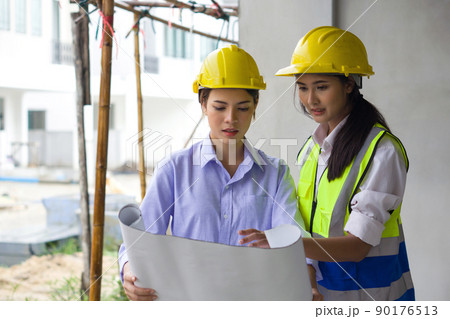 Young engineer in a construction helmet and safety vest explaining to project owner about a floor plan. Work environment of engineers at the construction site of housing projects. Young engineer in a construction helmet and safety vest explaining to project owner about a floor plan. Work environment of engineers at the construction site of housing projects. 90176513