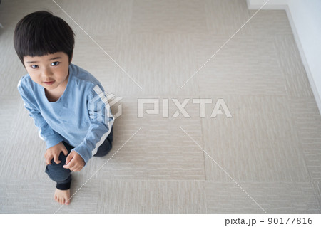 4歳男児が、陽当りのよい部屋のタイルカーペットに片膝をついてこちらを見ている 90177816