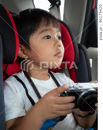 チャイルドシートに座り、カメラを持ちつつ、進行方向の景色を真剣な眼差しで見ている3歳男児 90179420
