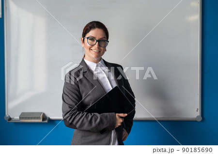 Beautiful woman in a suit with a digital tablet in her hands. A smiling female business coach with glasses stands in a conference room near a white board. Workshop at the office. 90185690