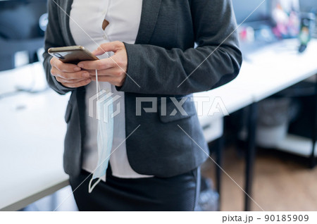 Business woman in a white shirt has taken off a medical mask and is typing on a smartphone. Faceless female office clerk texting over a break at work. End of quarantine. Victory over the coronavirus. Business woman in a white shirt has taken off a medical mask and is typing on a smartphone. Faceless female office clerk texting over a break at work. End of quarantine. Victory over the coronavirus. 90185909