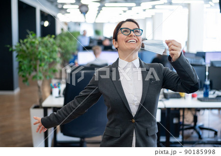 A happy female office worker in a suit takes off her medical mask and breathes freely with full breasts. A smiling woman takes off virus protection. End of quarantine. Victory over the coronavirus. A happy female office worker in a suit takes off her medical mask and breathes freely with full breasts. A smiling woman takes off virus protection. End of quarantine. Victory over the coronavirus. 90185998