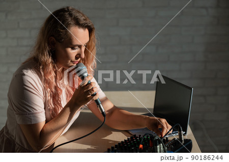 A woman sings into a microphone and plays online. A female blogger is recording a song using a synthesizer with a laptop. 90186244