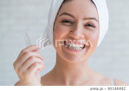 A woman with a towel on her head holds a whitening mouth guard for teeth. The girl aligns her teeth with the help of transparent night removable retainers. Orthodontic device for a perfect smile. 90186882