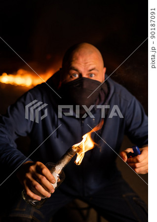 A masked man is holding a burning bottle. Molotov cocktail. A masked man is holding a burning bottle. Molotov cocktail. 90187091