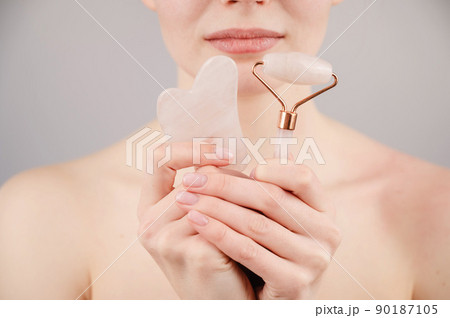 Caucasian woman holding pink roller massager and gouache scraper on white background. Caucasian woman holding pink roller massager and gouache scraper on white background. 90187105