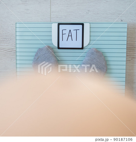 Top view of women's feet in gray socks on a floor scale. The inscription on the screen is fat. An obese man measures his weight. Naked big belly. 90187106
