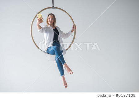 Caucasian woman gymnast on an aerial hoop takes a selfie on a smartphone.  90187109