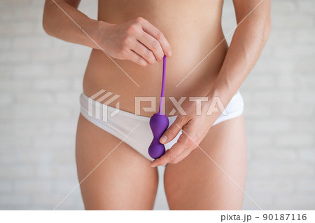 Faceless woman in white panties and with a bare tummy holds a kegel trainer. Latex vaginal vibrator for training the pelvic floor muscles with an antenna. The device for imbuilding. Women Health. 90187116