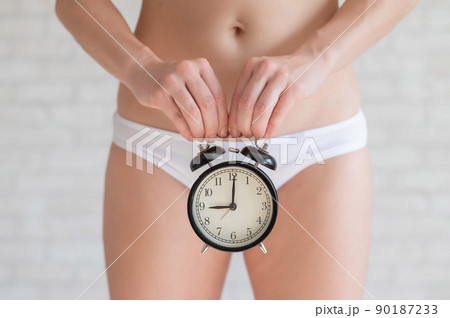 A woman in white panties with a bare belly holds a classic alarm clock. Female biological clock is ticking. Fertility. It's time to have a baby. 90187233