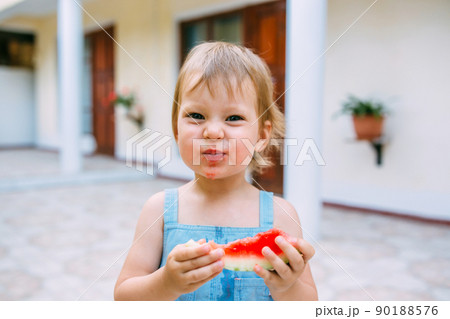 Little cute cheerful girl eating a slice of watermelon close up. 90188576