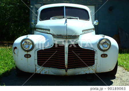 Head-on shot of a clean white vintage car flanked by grass on either side 90189063