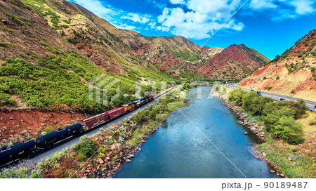 Train driving through valley of red mountains with river 90189487