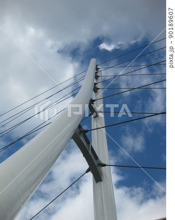 Worm's eye view of a white triangular bridge with suspension cables crisscrossing a blue and cloudy sky Worm's eye view of a white triangular bridge with suspension cables crisscrossing a blue and cloudy sky 90189607