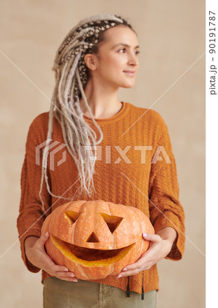 Attractive young craftswoman with dreads holding carved pumpkin and looking away, Halloween concept Attractive young craftswoman with dreads holding carved pumpkin and looking away, Halloween concept 90191787
