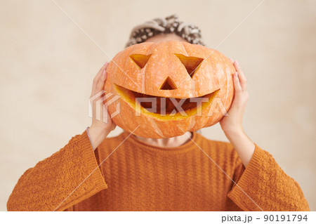 Unrecognizable woman in brown sweater holding funny pumpkin against face Halloween party Unrecognizable woman in brown sweater holding funny pumpkin against face Halloween party 90191794