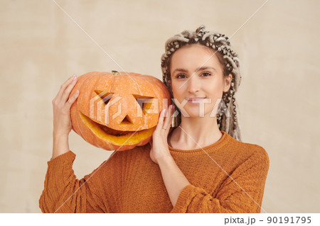 Portrait of smiling hipster young woman with white dreads posing with jack-o-lantern on shoulder against isolated background, Halloween concept Portrait of smiling hipster young woman with white dreads posing with jack-o-lantern on shoulder against isolated background, Halloween concept 90191795