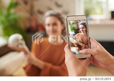 Hands taking photo of pretty young woman with dreads posing with skull at Halloween party Hands taking photo of pretty young woman with dreads posing with skull at Halloween party 90191804