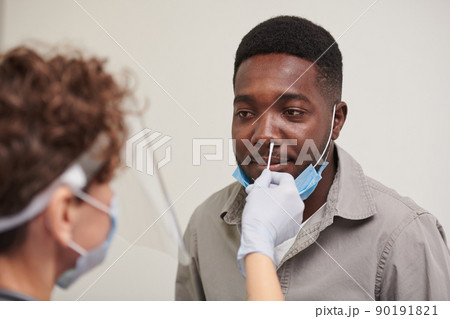 High angle medium close-up shot of unrecognizable doctor wearing protective masks testing African American male patient for viral disease 90191821