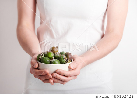 Horizontal medium section shot of unrecognizable woman wearing white clothes holding bowl full of pineapple guava fruits, copy space 90192422