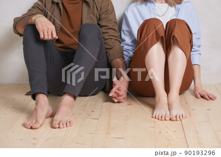 Lovely unrecognizable couple wearing casual clothes sitting relaxed on floor and holding hands, copy space 90193296