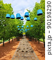 beautiful alley of even rows of trees, black benches, hanging, blue lamps in the park. Landscaping. Walkway made of tiles, paving stones 90198290