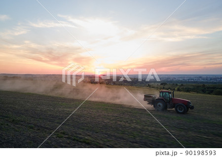 Tractor spraying fertilizers with insecticide herbicide chemicals on agricultural field at sunset 90198593