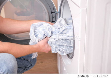 A man takes dried bed linen out of the dryer 90199202