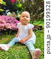 Smiling laughing happy girl in spring, summer against the backdrop of pink flowers, trees sits on the grass in the park, in a white dress and sneakers. Looking up with blue eyes 90199328