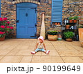 happy baby sits on porch front facade beautiful brick, Italian, Spanish house. Rustic terrace. large wooden blue door and shutters on window. child plays summer yard. 90199649