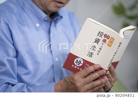 「投資」の本を読んで微笑むシニア男性の手元 90204851