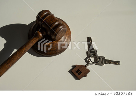 Keys with a keychain in the shape of a house and a judge's gavel on a white background. Keys with a keychain in the shape of a house and a judge's gavel on a white background. 90207538