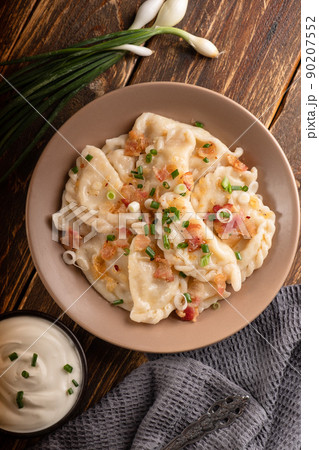 Potato dumplings with sour cream on the wooden table. Traditional ukrainian food. Varenyky, vareniki, pierogi, pyrohy - dumplings with filling. 90207552
