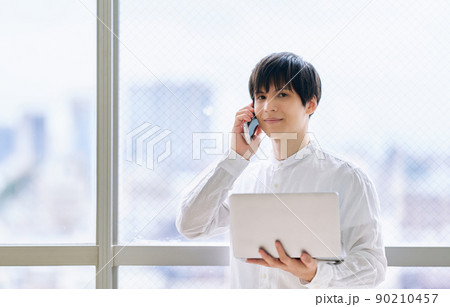 スマホとノートパソコンを持つ若い男性 90210457