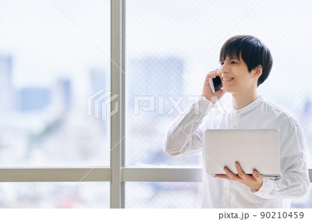 スマホとノートパソコンを持つ若い男性 90210459