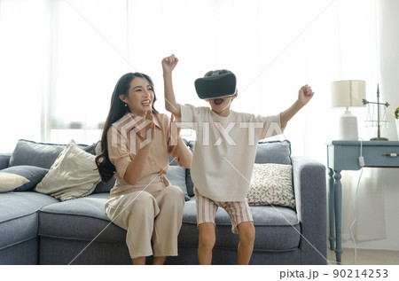 Smiling mother looking son playing games using virtual reality headset(VR) at home. Technology future concept. 90214253