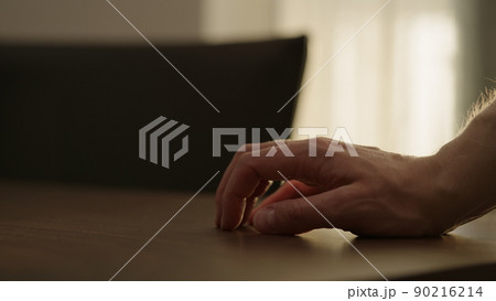 Man hand finger tapping on a walnut table with sunlight from a window behind 90216214